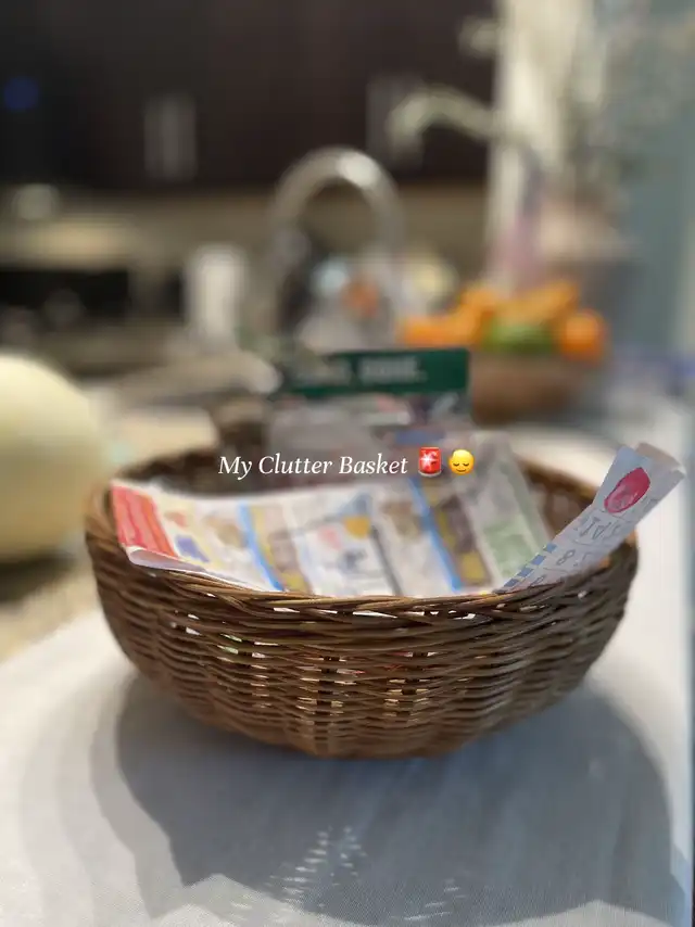 A brown woven basket on a table, partially filled with various papers and coupons, labeled "My Clutter Basket."